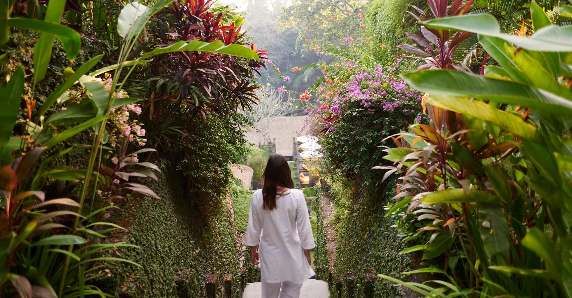 Woman descending the stairs flanked by gardens at Sukhavati Ayurvedic Wellness Retreat Bali.