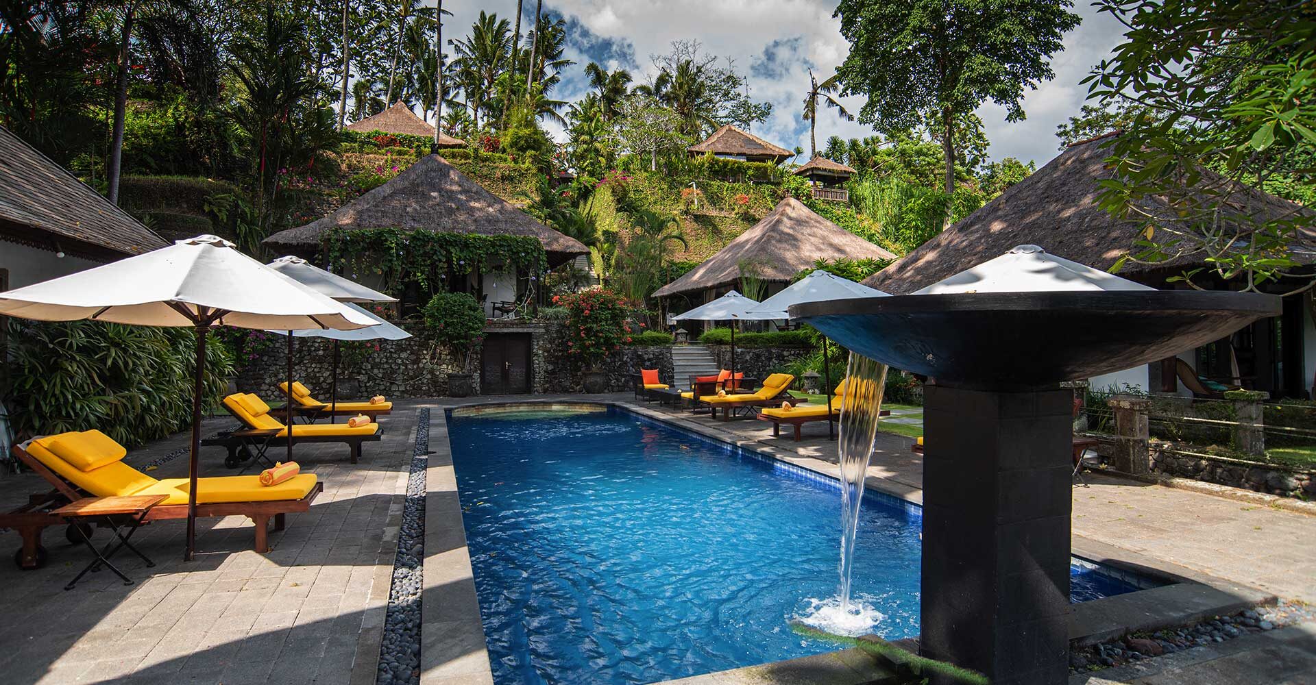 Pool relaxation area with chairs and fountain in the grounds of Sukhavati Ayurvedic Wellness Retreat in Bali. 
